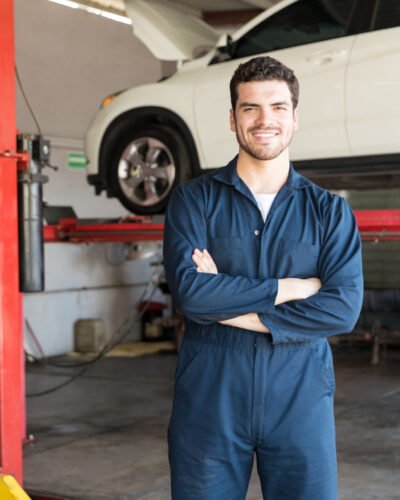 Smiling mechanic in uniform standing with hands folded in auto shop