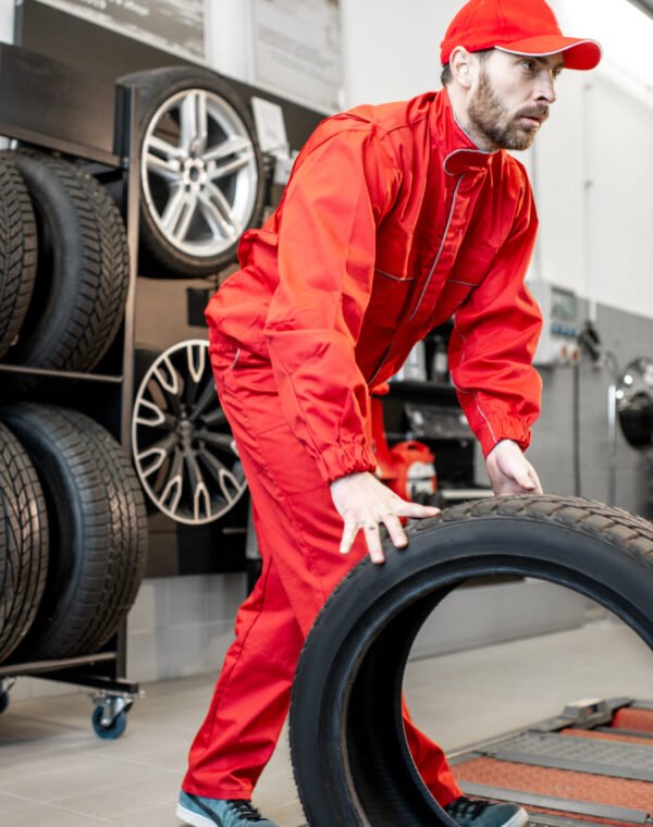 Worker with new tires at the shop or service Car service worker in red uniform carrying new tires at the tire mounting service or shop